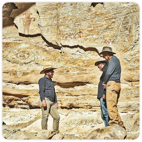 Photograph of people standing in front of a large sandstone wall.